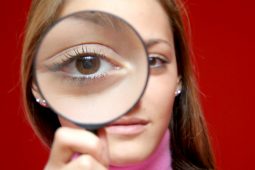 Nice and beautiful girl holding magnifining lens in front of her eye and making photo interesting for some investigation design