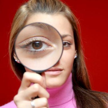 Nice and beautiful girl holding magnifining lens in front of her eye and making photo interesting for some investigation design